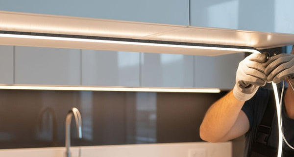 A person installing an LED strip under a kitchen cabinet