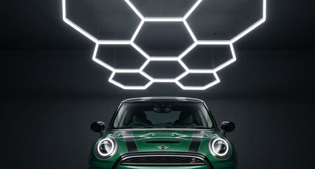 A green and black glossy small car under a hexagon lighting setup inside a dark parking spot.