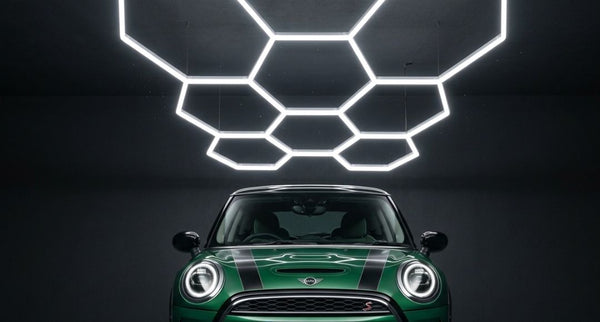 A green and black glossy small car under a hexagon lighting setup inside a dark parking spot.