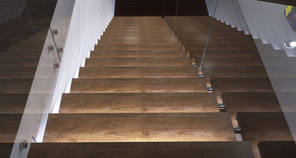 A top view of a wooden staircase inside a modern house with each step illuminated by LED lights.