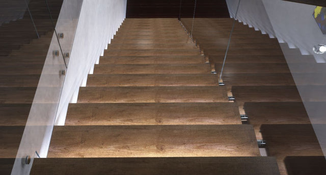 A top view of a wooden staircase inside a modern house with each step illuminated by LED lights.
