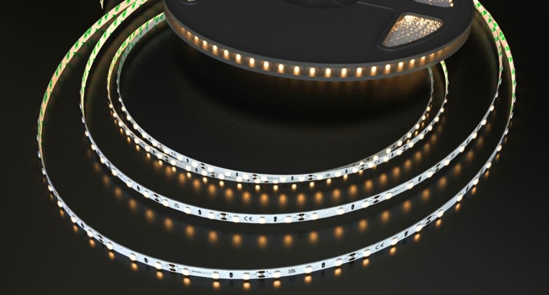 A roll of LED strip light on a dark reflective surface glowing with a warm white tone.