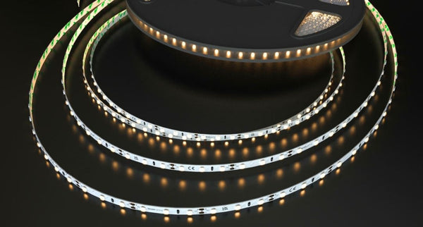 A roll of LED strip light on a dark reflective surface glowing with a warm white tone.