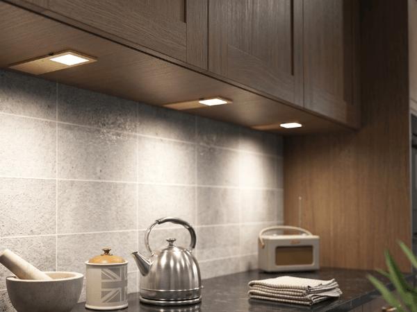 Three brass coloured under cabinet lights installed below dark wood kitchen wall cabinets, lighting the worktop below.