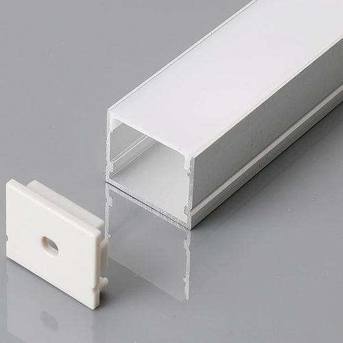 A close-up shot of a silver LED profile with a milky white diffuser cover and a white end cap on a grey reflective surface.