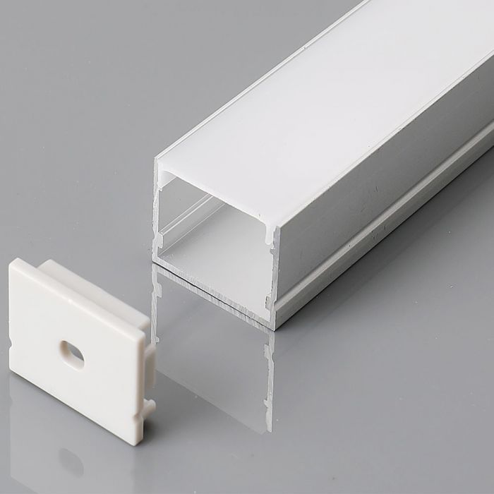 A close-up shot of a silver LED profile with a milky white diffuser cover and a white end cap on a grey reflective surface.