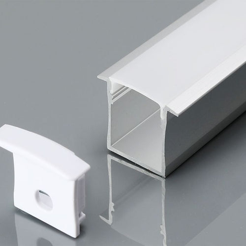 A close-up image of the recessed profile with a white diffuser and an end cap, laid on a reflective grey surface.