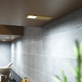The ultra-slim brushed brass under cabinet light mounted under a wooden surface, glowing a cool white glow.