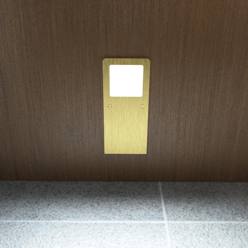 Front view of the slim under cabinet light with a brushed brass finish, installed under a wooden surface, and glowing with a cool white tone.