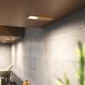The ultra-slim brushed brass under cabinet light mounted under a wooden surface, glowing a natural white glow.
