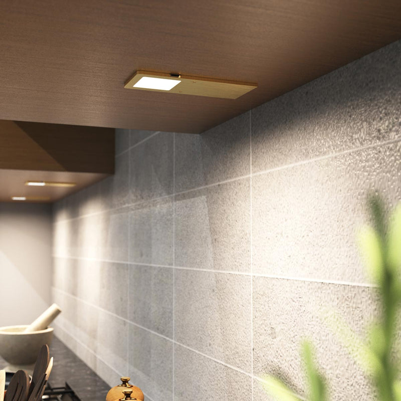 The ultra-slim brushed brass under cabinet light mounted under a wooden surface, glowing a natural white glow.