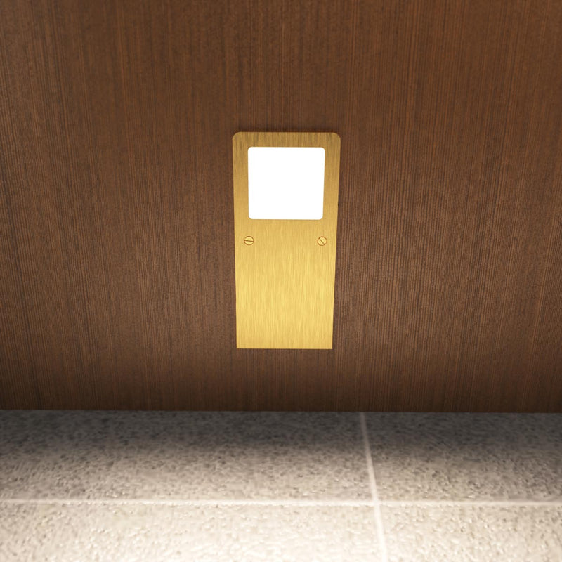 Front view of the slim under cabinet light with a brushed brass finish, installed under a wooden surface, and glowing with a natural white tone.