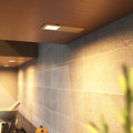 The ultra-slim brushed brass under cabinet light mounted under a wooden surface, glowing a warm white glow.
