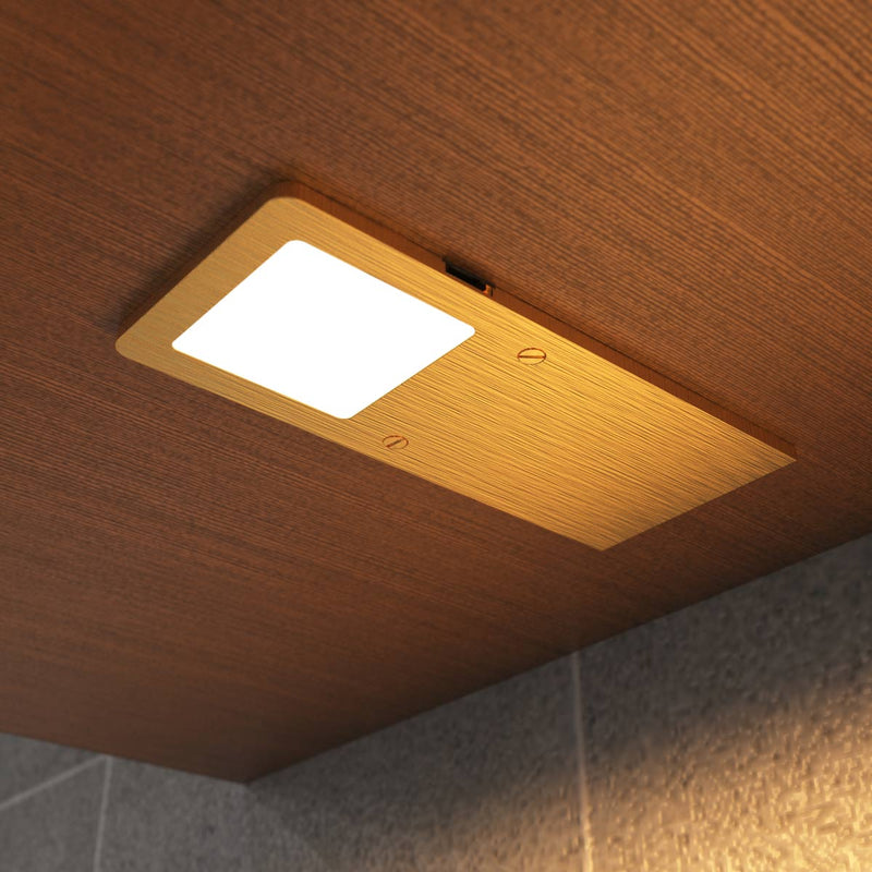 Warm white glow on the ultra-slim brushed brass under cabinet light mounted under a wooden surface.