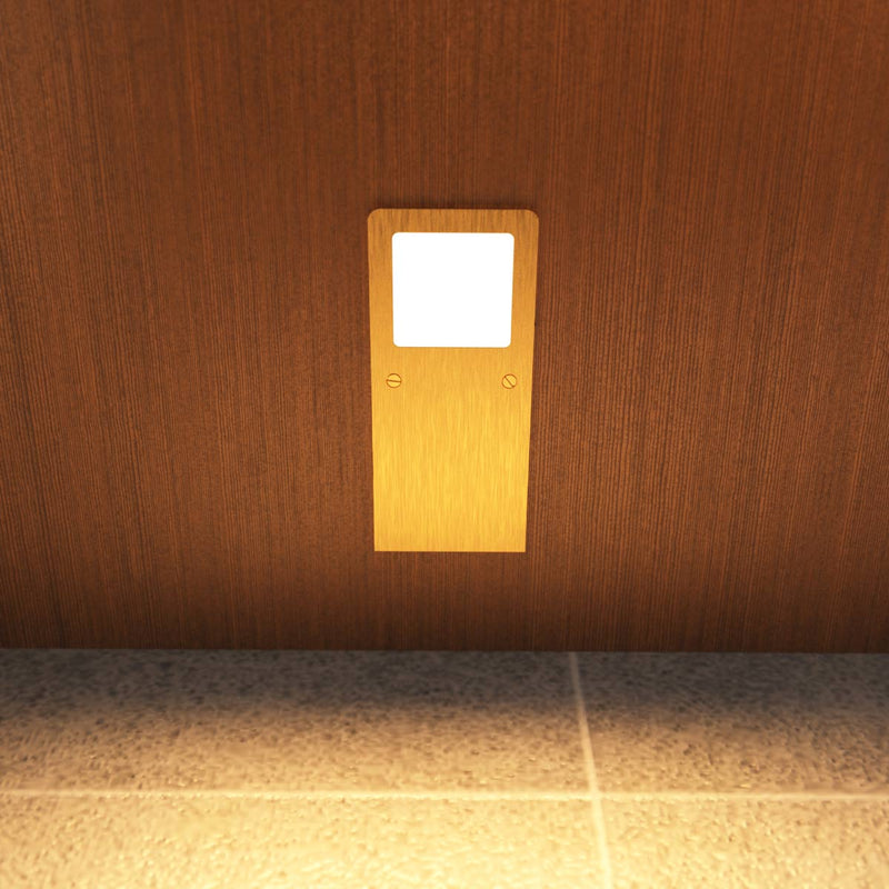 Front view of the slim under cabinet light with a brushed brass finish, installed under a wooden surface, and glowing with a warm white tone.
