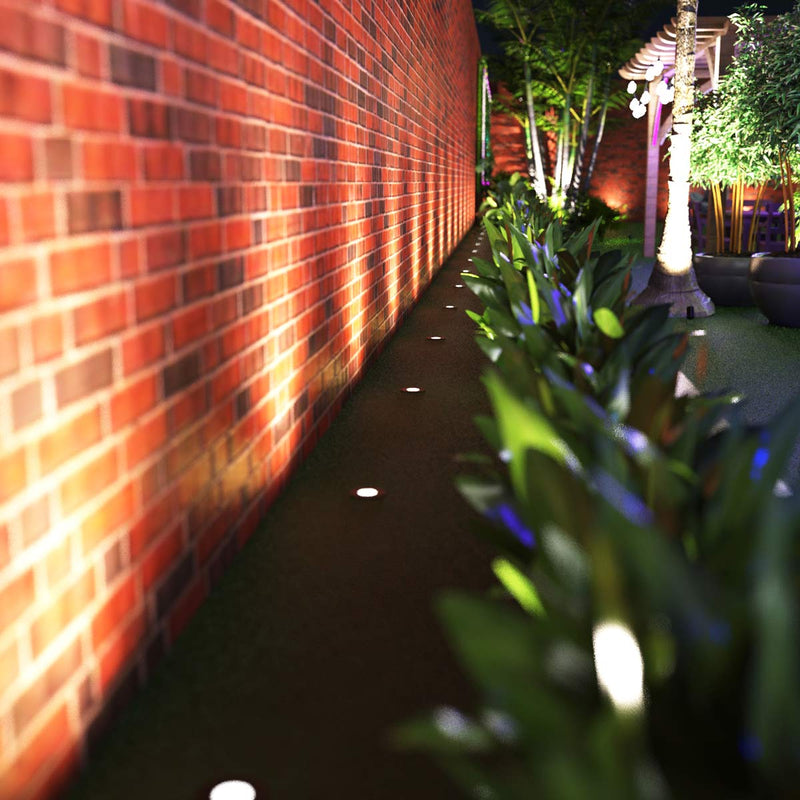 Close up of a garden with ground lights lined across a brick wall